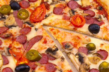 Salamlı, domatesli, mantarlı, zeytinli ve biberli ince hamurlu pizza. Kesilmiş bir pizza. Yakın çekim, üst görünüm.