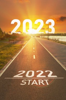 Yeni yıl 2022 başlangıç konsepti. 2022 ve 2023 yılları, güneşin parlak ışınlarında, boş spor yolundaki asfaltta yazılıdır. Gelecekte vizyon ve eylem için motivasyon kavramı
