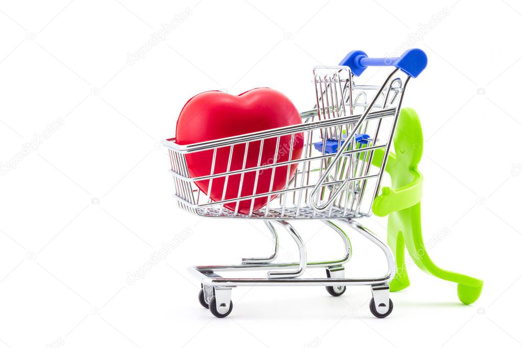 Green plastic toy abstract figure of man pushing shopping trolley with big red heart inside. Greeting card for Valentine's day. Ideas for healthcare, shopping in pharmacies or supermarket sales