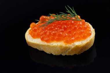 Siyah arka planda izole edilmiş kırmızı havyarlı sandviç. Taze dereotlu buğday ekmeğine tuzlu somon havyarı. Parlak bir yüzeyde yansıma