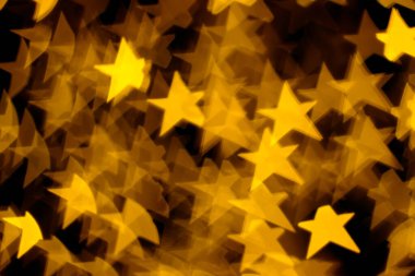 Golden stars lights bokeh on dark background. Concept of Christmas and Happy New Year. Abstract holiday background with copy space.