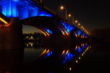 Rusya 'nın Krasnoyarsk kentindeki Yenisei Nehri' nden geçen mavi ve altın renginde bir köprü. Gece şehir ışıkları