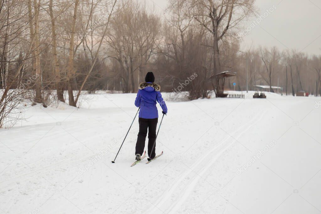 Woman skier walking by the snow in a winter city park. Winter sports and leisure outdoors. Winter holidays on weekends