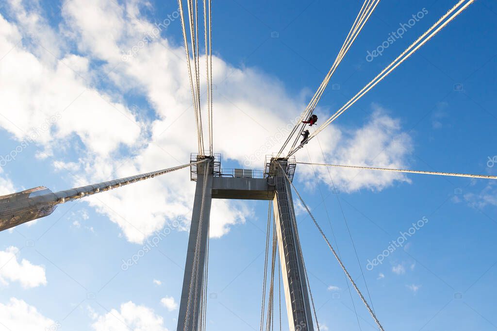 industrial climbers repair lighting equipment on a suspension bridge at high heights against blue sky background.
