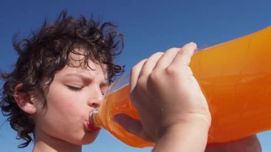 Kıvırcık çocuk büyük şişeden portakal suyu içiyor.