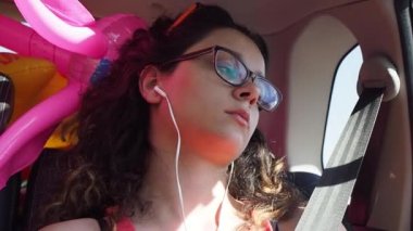 Kıvırcık gözlüklü genç kızın hareket halindeki arabada oturduğu görüntüler.