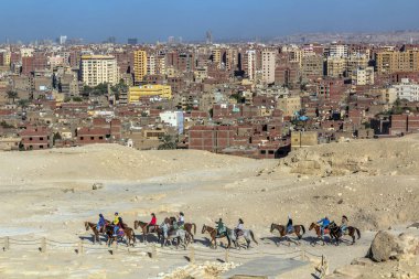 CAIRO, EGYPT - 28 HAZİRAN 2019: Turistler Giza şehrinin arka planına sahip piramitlerin önünde ata biniyorlar, Mısır