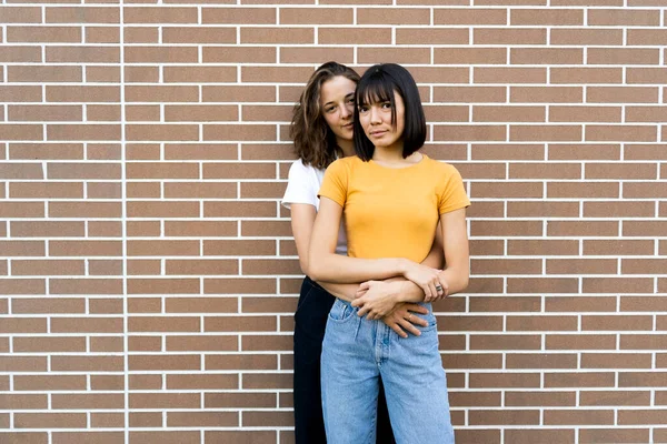 Young Woman Embracing Girlfriend While Standing Front Brick Wall — Stock Photo, Image