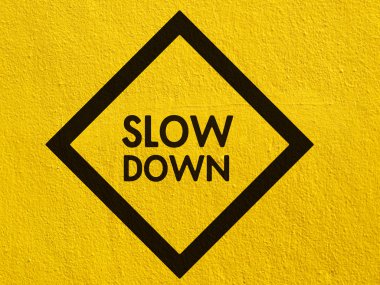 Slow Down yellow road sign painted on a stucco wall outside clipart