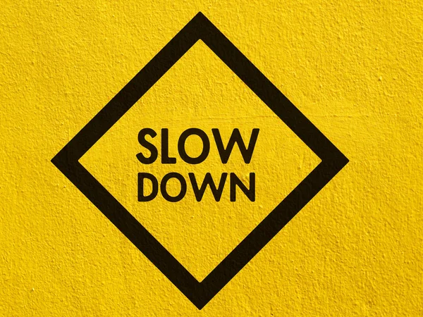 Slow Down yellow road sign painted on a stucco wall outside — Stock Photo, Image