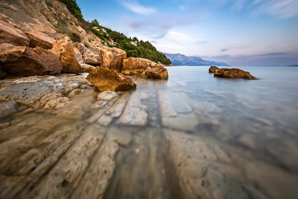 Rotsachtig strand en transparante Adriatische Zee in de buurt van omis in de evenin — Stockfoto
