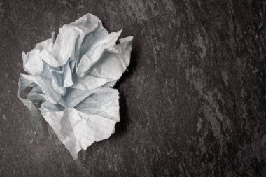 Masaya buruşmuş ve yırtılmış kağıt. Defterin bir parçası parçalanmış. Kağıt çöpü. Bir sepet dolusu not. Buruşmuş kağıt zemin üzerinde not defteri ve kalem.