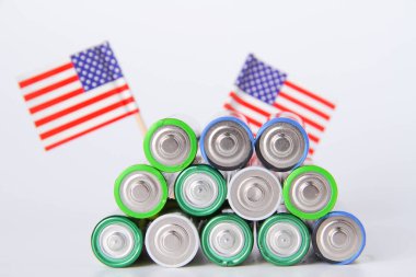 Batarya. ABD bayrağının arka planında bir sürü pil var. Alkali ve alkali pil. Çinko ve tuz bataryası. Lityum ithalatı. Çöp öğütücü.