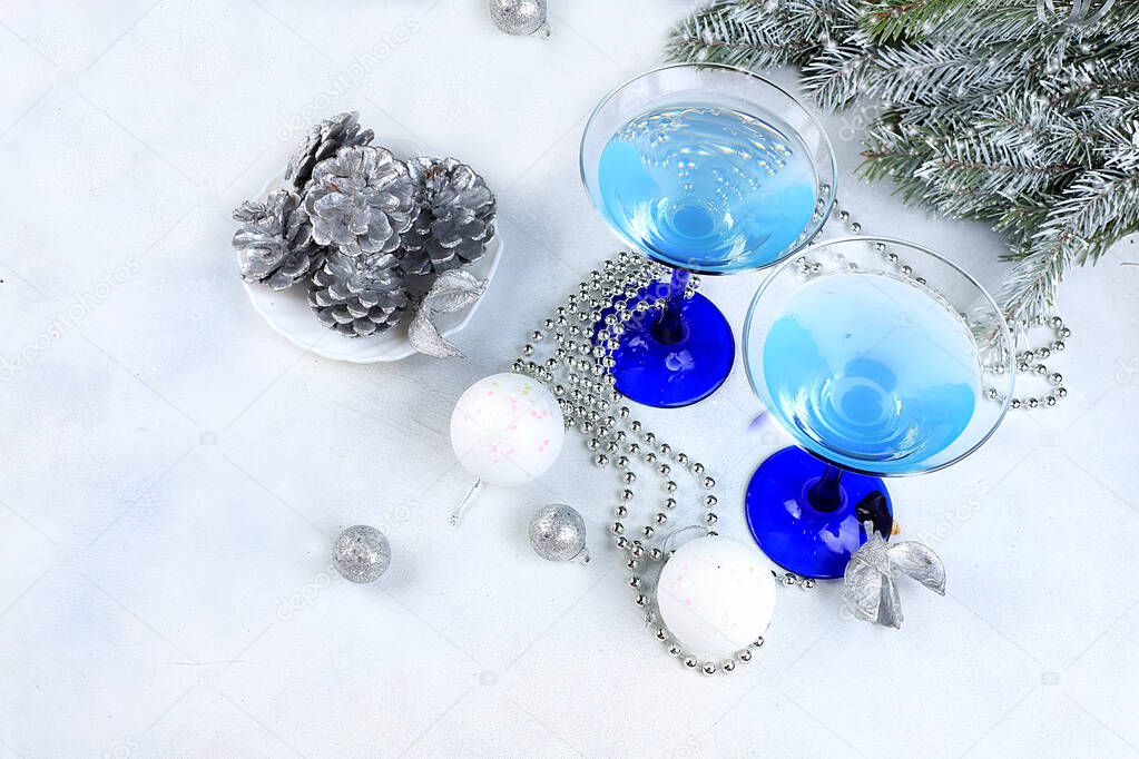 Blue alcoholic cocktail with lemonade, champagne or martini in glasses on a festive christmas table with fir branches and decorations, bar concept, alcoholic drinks at a party, selective focus