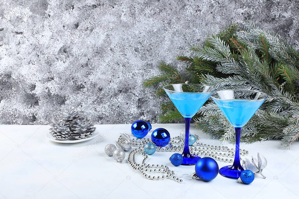 Blue alcoholic cocktail with lemonade, champagne or martini in glasses on a festive christmas table with fir branches and decorations, bar concept, alcoholic drinks at a party, selective focus