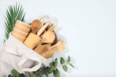 Güneşli bir masada, bir torba içinde, çevre dostu yemekler. Kağıt bardaklar, tabaklar, kağıt peçeteler, barbekü pipetleri, tahta çatallar, kaşıklar ve bıçaklar, maket, sağlıklı yaşam tarzı konsepti, sıfır atık. Plastik yok, seçici odaklanma