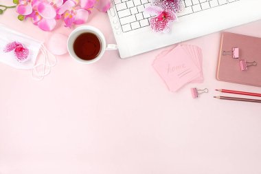 Modern kadın masaüstü, ev ofisi. Bir bilgisayar, bir fincan çay, tıbbi maske ve ışık masasında bahar çiçekleri. Asgari iş konsepti, ev konforu, üst görünüm, düz konum, metin için alan.