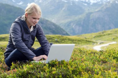 sarışın genç kadın dağ çayır içinde laptop ile oturuyor.