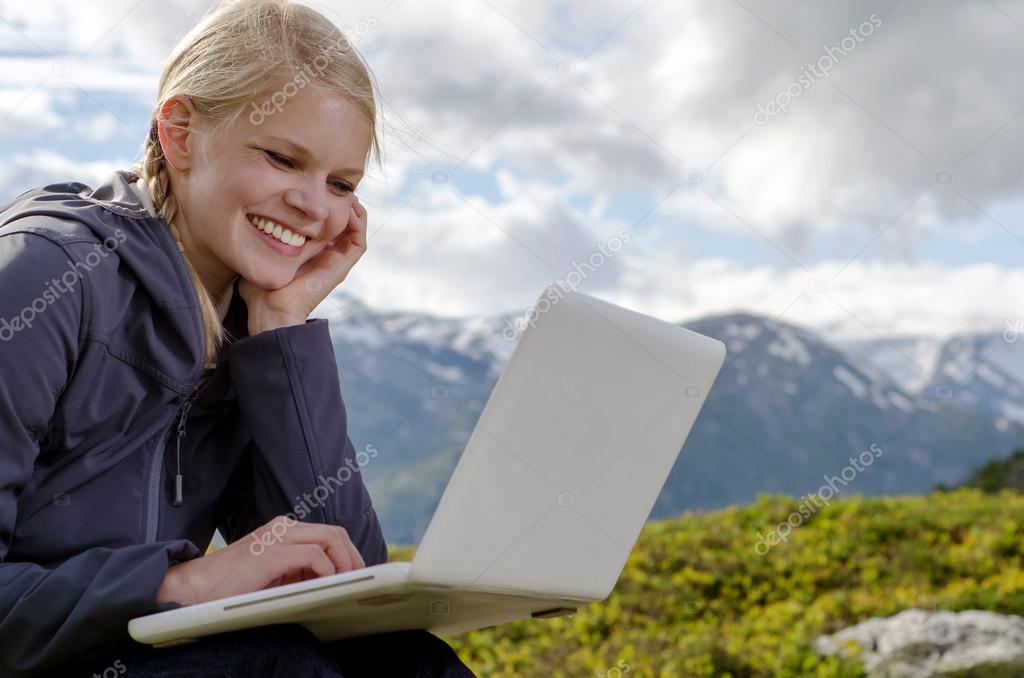 young blond woman with a laptop before a mountain landscape