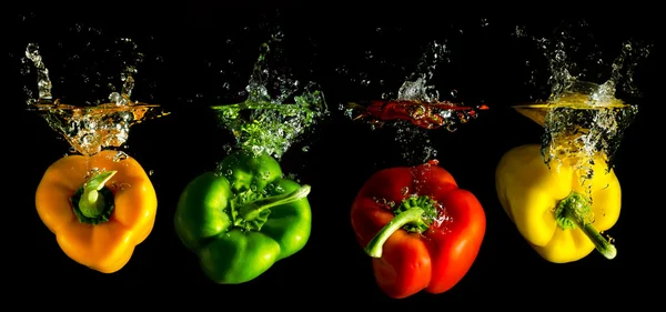 Quatre paprika de plusieurs couleurs tombant dans l'eau — Photo