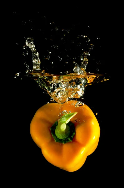 Oranje peper valt in het water Stockfoto