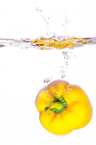 Yellow paprika pepper splashes into water before white — Stock Photo, Image