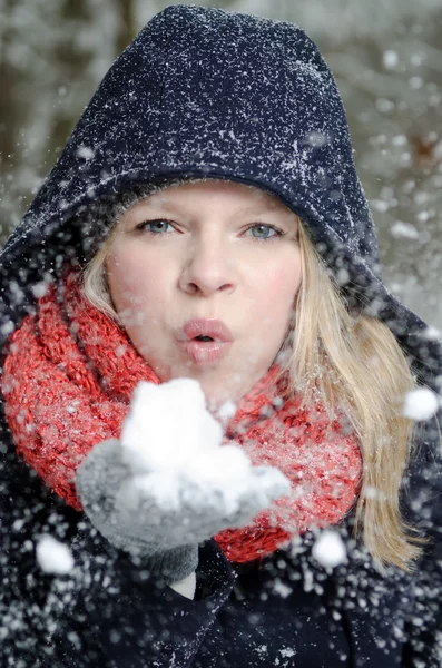 Junge blonde Frau bläst in eine Handvoll Schnee — Stockfoto