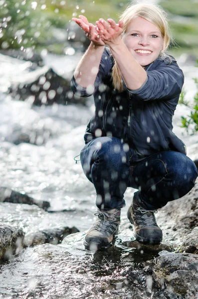 Een wandel jonge blonde vrouw verfrist zich in aan een beek — Stockfoto