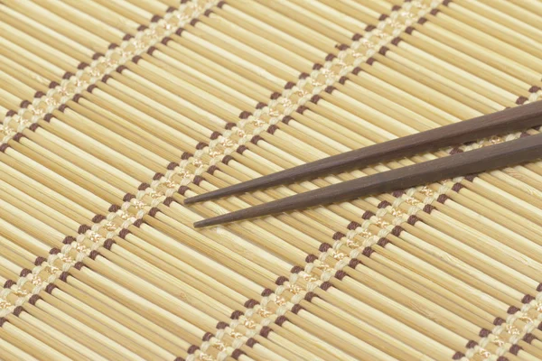 Dark wooden chopsticks on bamboo mat — Stock Photo, Image