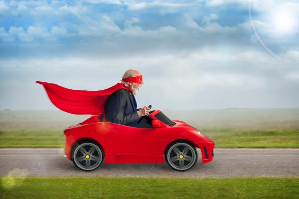 Superherói sênior dirigindo um carro esporte de brinquedo Fotos De Bancos De Imagens