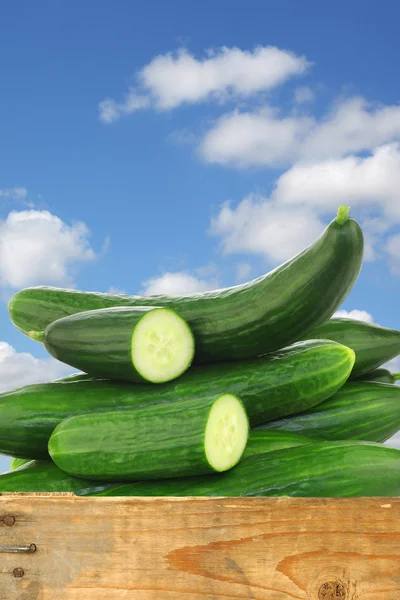 Fresh cucumbers and some cut pieces in a wooden crate — Stock Photo, Image