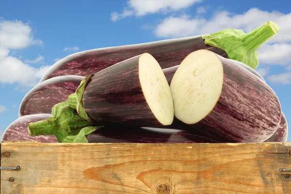 Gemischte Auberginen und eine geschnittene Aubergine in einer Holzkiste — Stockfoto