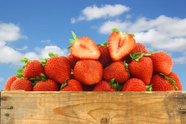 Fresh strawberries and a cut one in a wooden crate — Stock Photo, Image