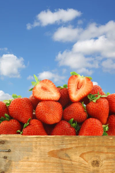 Fresh strawberries and a cut one in a wooden crate — Stock Photo, Image
