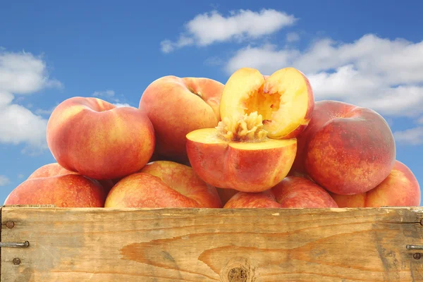 Fresh wild (flat) nectarines and a cut one in a wooden crate — Stock Photo, Image