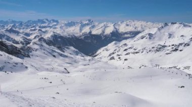 Bir çok kayakçı ve snowboardcu dağ yamacında kayak yapıyor.