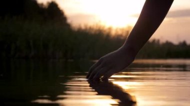 Yüzey suyuna dokunur ve gün batımının arka planında bir avuç avuçla ortaya çıkar.