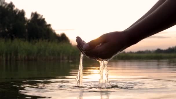 Mujer toca superficie agua y recoge palma de mano fondo de puesta del sol — Vídeos de Stock