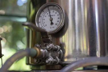 round industrial thermometer with pointer and scale in degrees and fahrenheit and a blurred quick-lock valve in the foreground