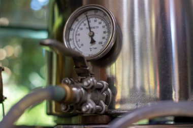 round industrial thermometer with pointer and scale in degrees and fahrenheit and a blurred quick-lock valve in the foreground