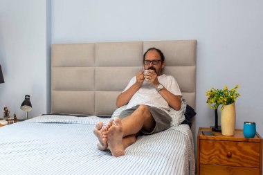 Son sınıf öğrencisi yatakta oturup kahve içiyor.