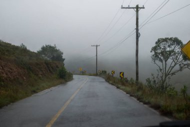 Sisli bir günde ağaçların olduğu kırsal bölgede çift yönlü yol. Araba yok. 