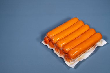 Mavi arka planda üretici tarafından plastiğe sarılmış sosis.