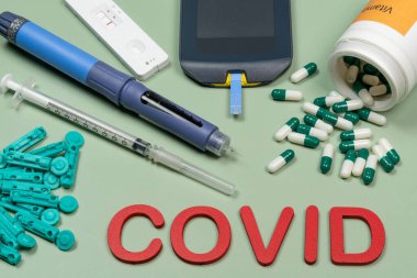 Kan şekerini, D vitamini kutusunu ve yeşil arka planda yazılmış Covid kelimesini, üst görünümü ölçmek için bir aygıt