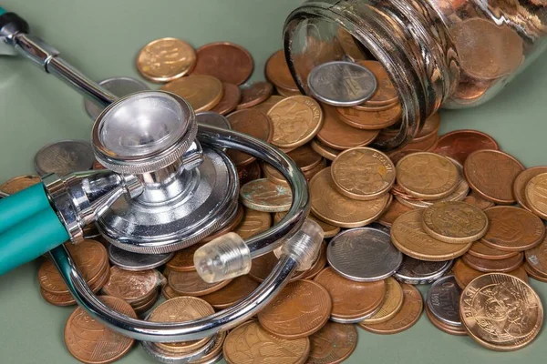 The concept of economy and medicine costs health. Pile of real coins and stethoscope. Economic health isolated on green background.