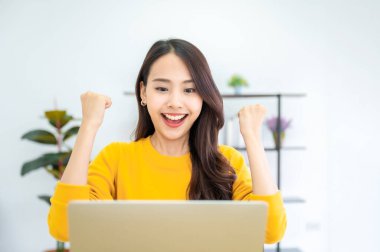 Heyecanlı bir kadın, online başarı kutlaması yapıyor. Başarılı bir başarı elde ediyor. Asyalı genç bir kadın, iyi e-posta haberlerinden memnun.