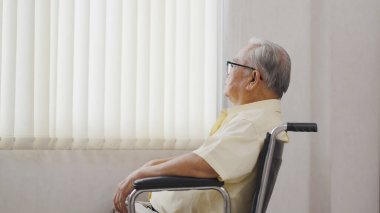Yaşlı Asyalı bir adam tekerlekli sandalyede oturur ve pencereden dışarı bakar. Sağlık ve sigorta, emeklilik kavramı