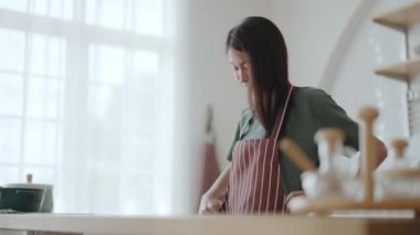 Önlük giyip mutfak odasında duran mutlu Asyalı kadın. Güzel bayan gülümsüyor ve kameraya bakıyor. Kendinden emin hissediyor.
