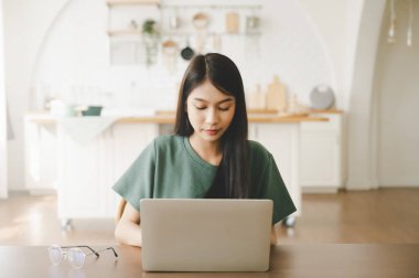 Ev bilgisayarında çalışan gülümseyen Asyalı genç kadın. Genç Asyalı öğrenci bilgisayar eğitimi alıyor, sanal eğitim alıyor, e-öğreniyor, evde online eğitim webinar izliyor.