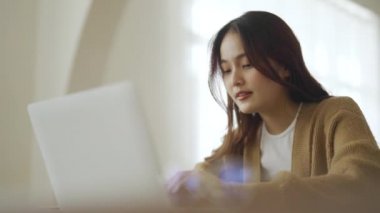 Ev bilgisayarında çalışan gülümseyen Asyalı genç kadın. Genç Asyalı öğrenci bilgisayar eğitimi alıyor, sanal eğitim alıyor, e-öğreniyor, evde online eğitim webinar izliyor.